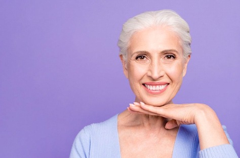 Smiling woman on purple background with dental bridges in Indianapolis